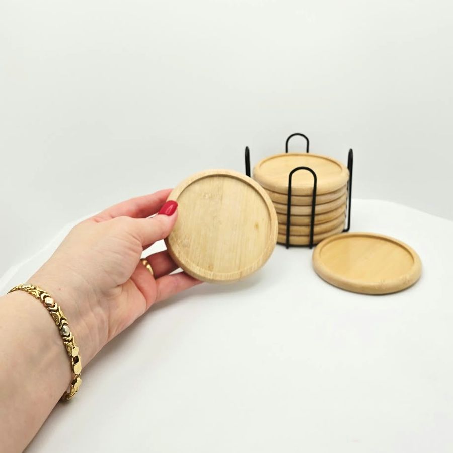 My hand holding a bamboo coaster, with another on the table and the rest in the holder