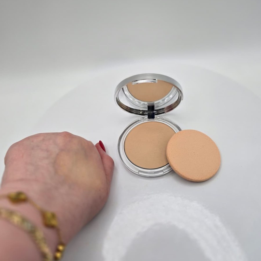 My open Clinique Stay-Matte compact with its sponge, next to a swatch of the powder on the back of my hand