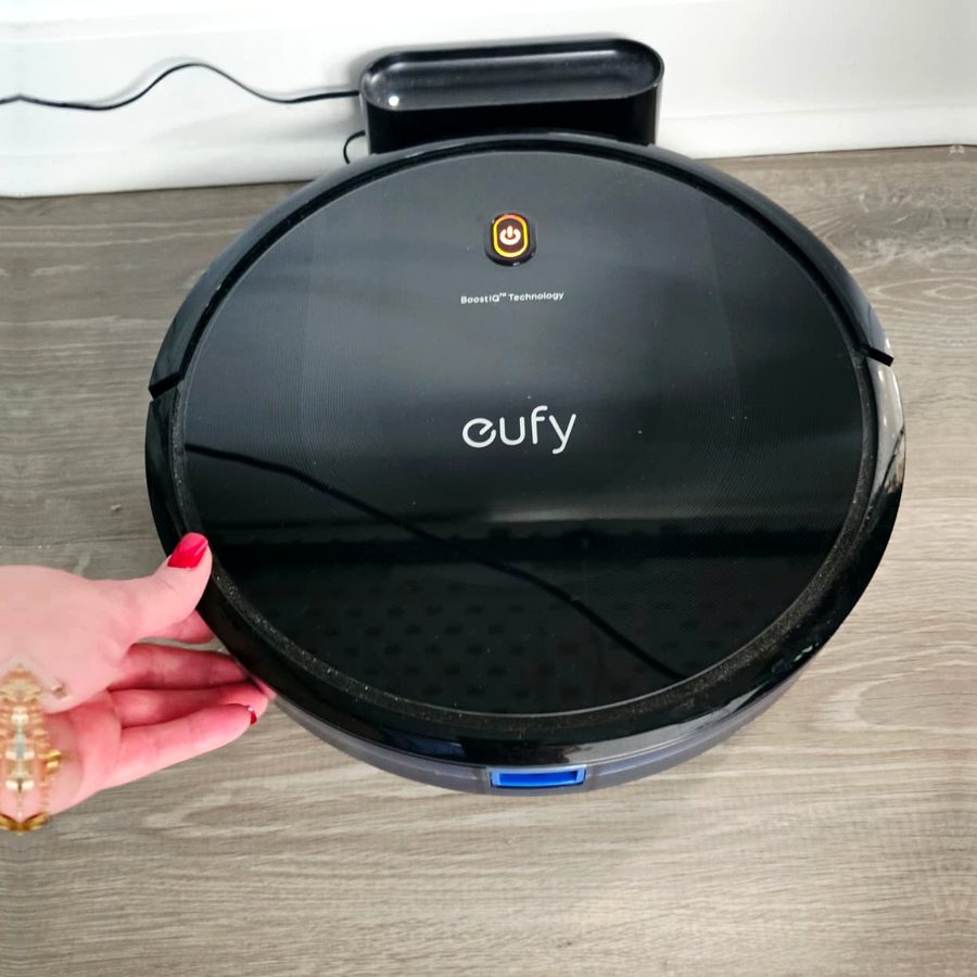 My hand on my eufy RoboVac 11S MAX, sitting in front of its charging base on my wood floor