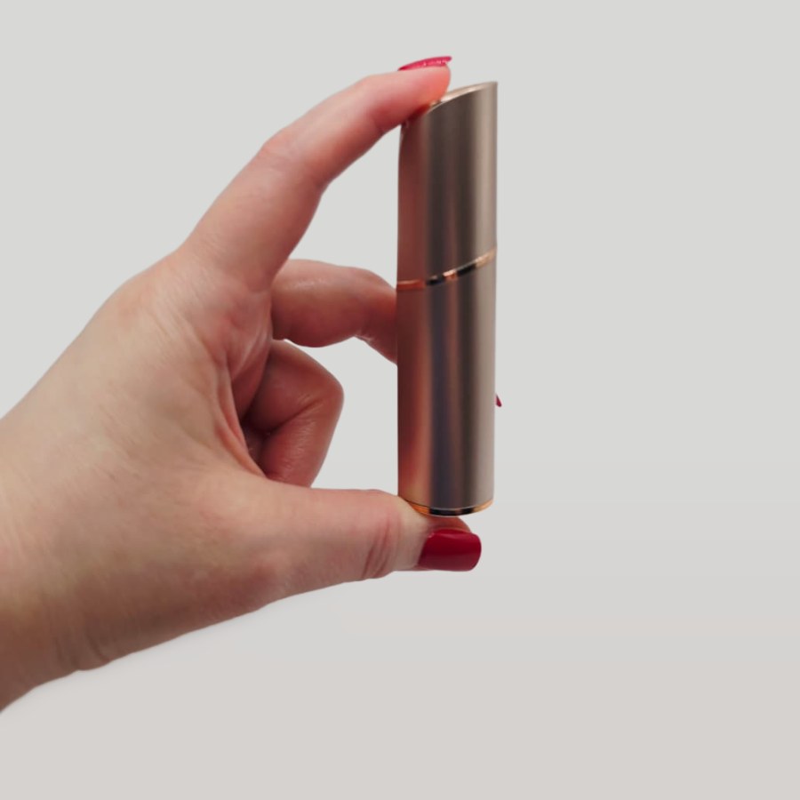 My Evolvique facial hair remover closed with its cap, held between two fingers, the size of a lipstick