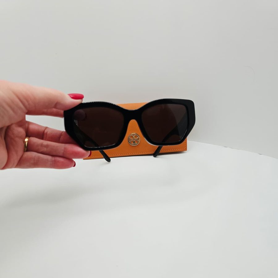 My hand holding my Tory Burch Kira sunglasses from the front, with the case behind them
