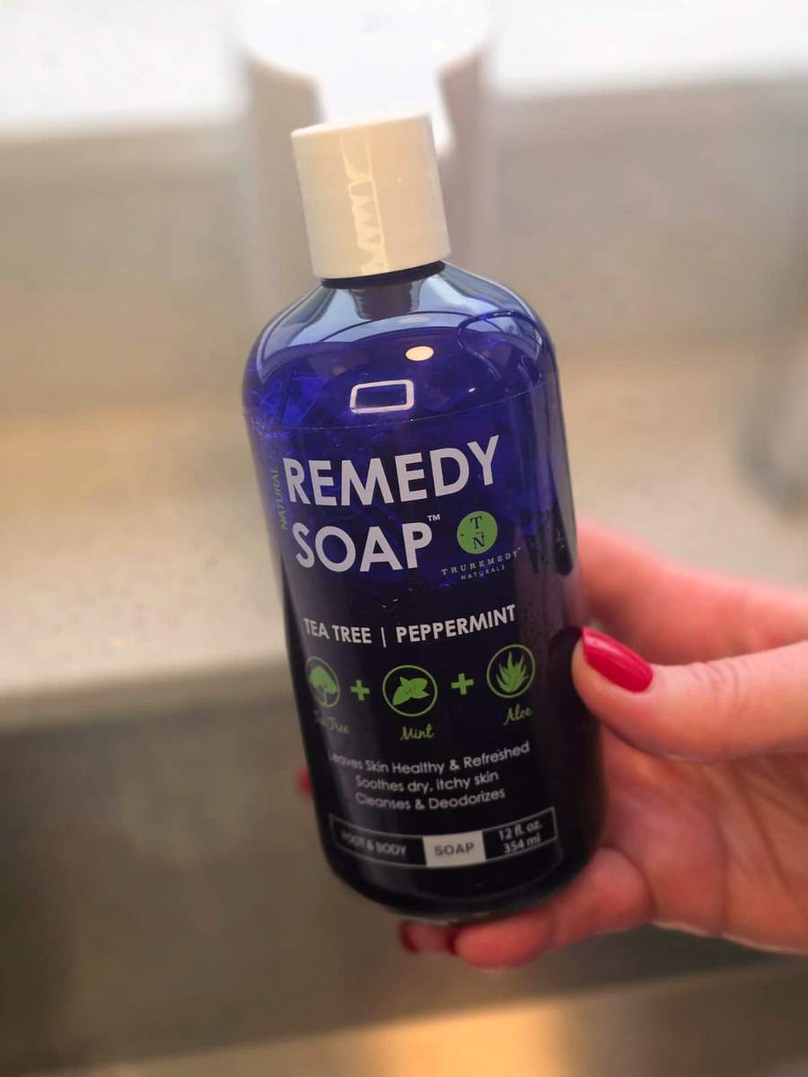 Holding the blue Remedy Soap bottle by my bathroom sink